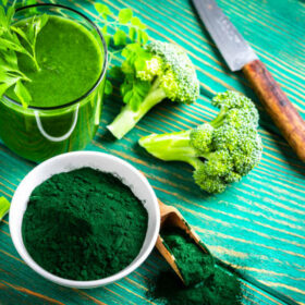 High angle view of a drinking glass filled with Spirulina smoothie and a bowl with Spirulina powder shot on green table. Some broccoli pieces and a kitchen knife are around the glass. High resolution 42Mp studio digital capture taken with Sony A7rII and Sony FE 90mm f2.8 macro G OSS lens
